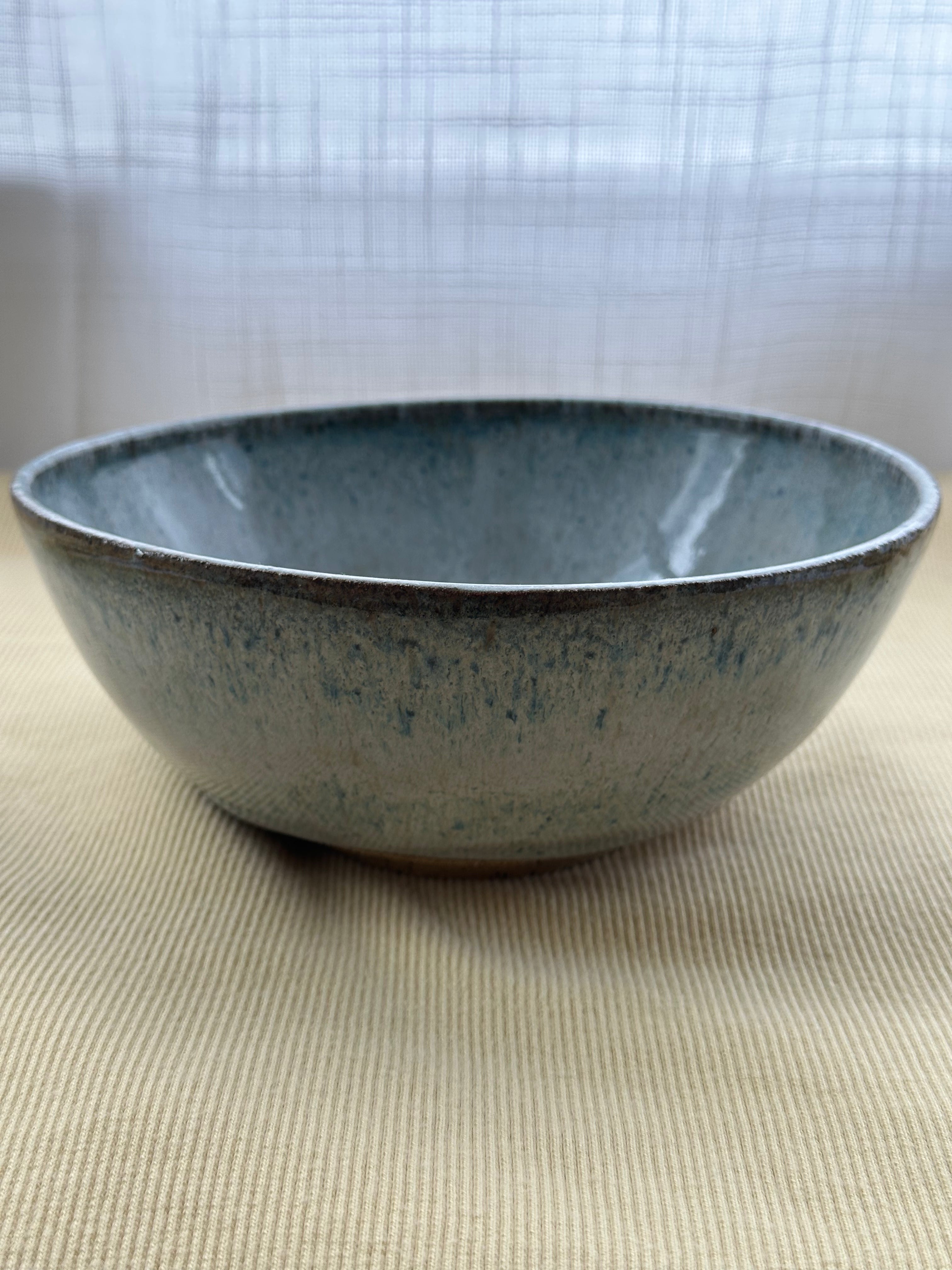 Blue ceramic bowl on a beige surface with a light gray curtain background
