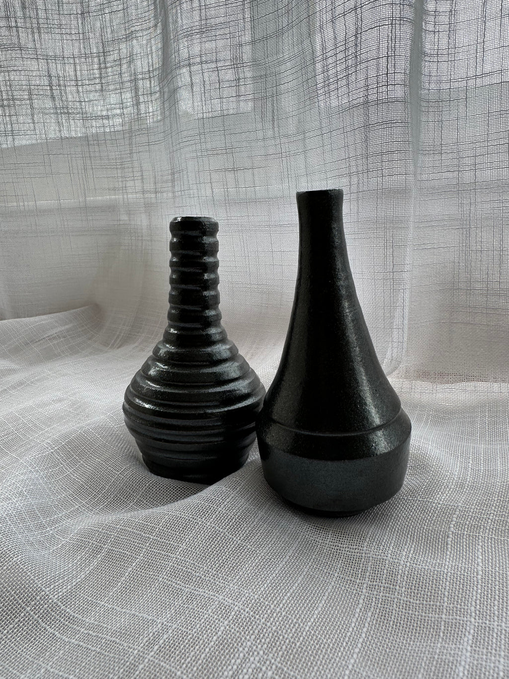 Two black ceramic vases on a textured gray fabric background