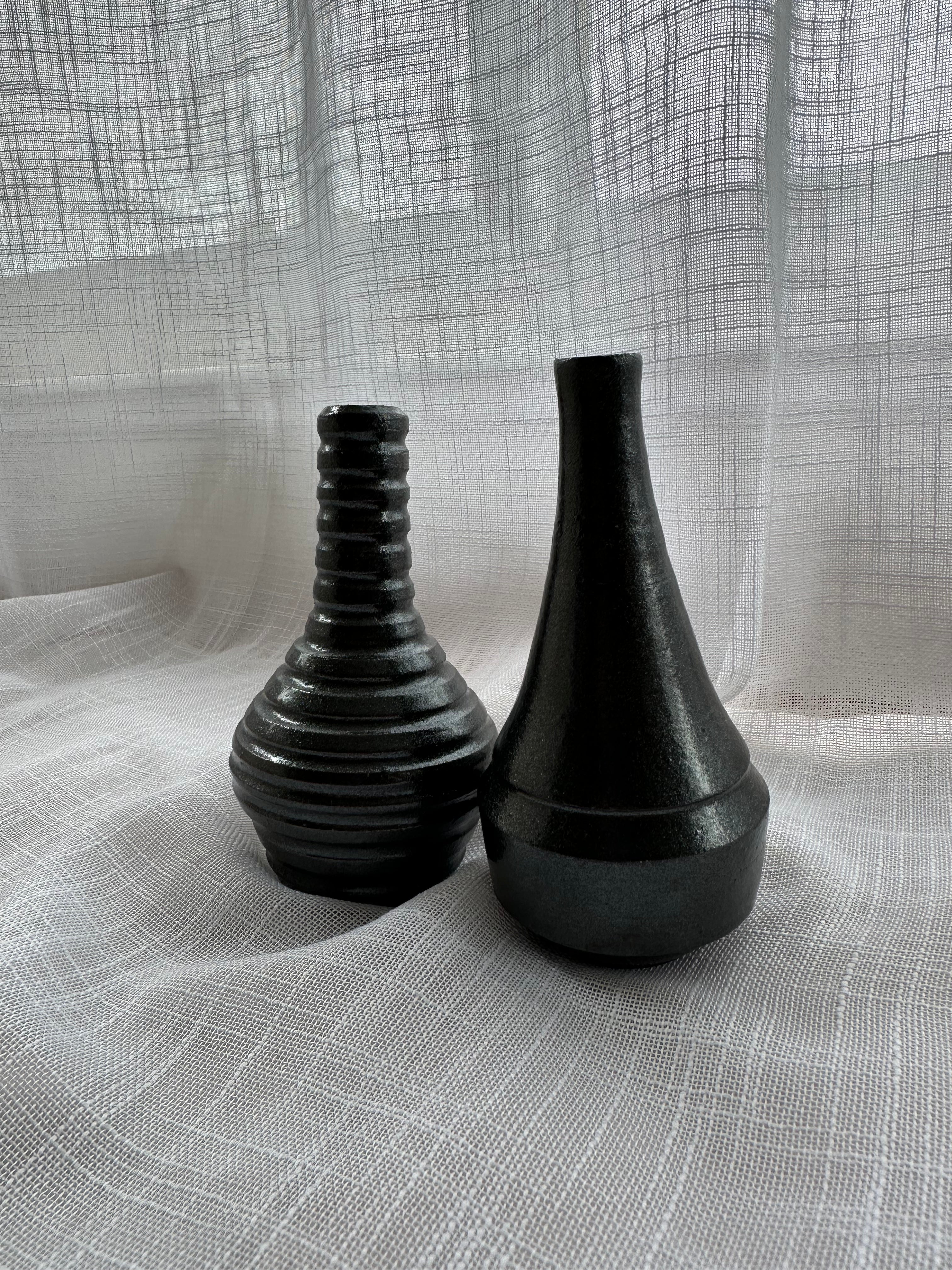 Two black ceramic vases on a textured gray fabric background