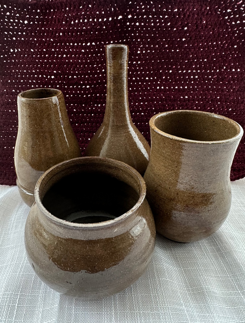 Set of four ceramic vases on a textured surface with a maroon woven pillow in the background.