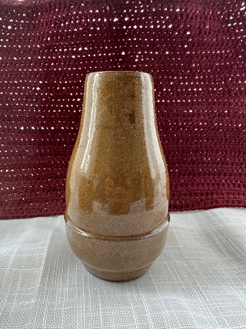 Brown ceramic vase on a textured surface with a maroon fabric background