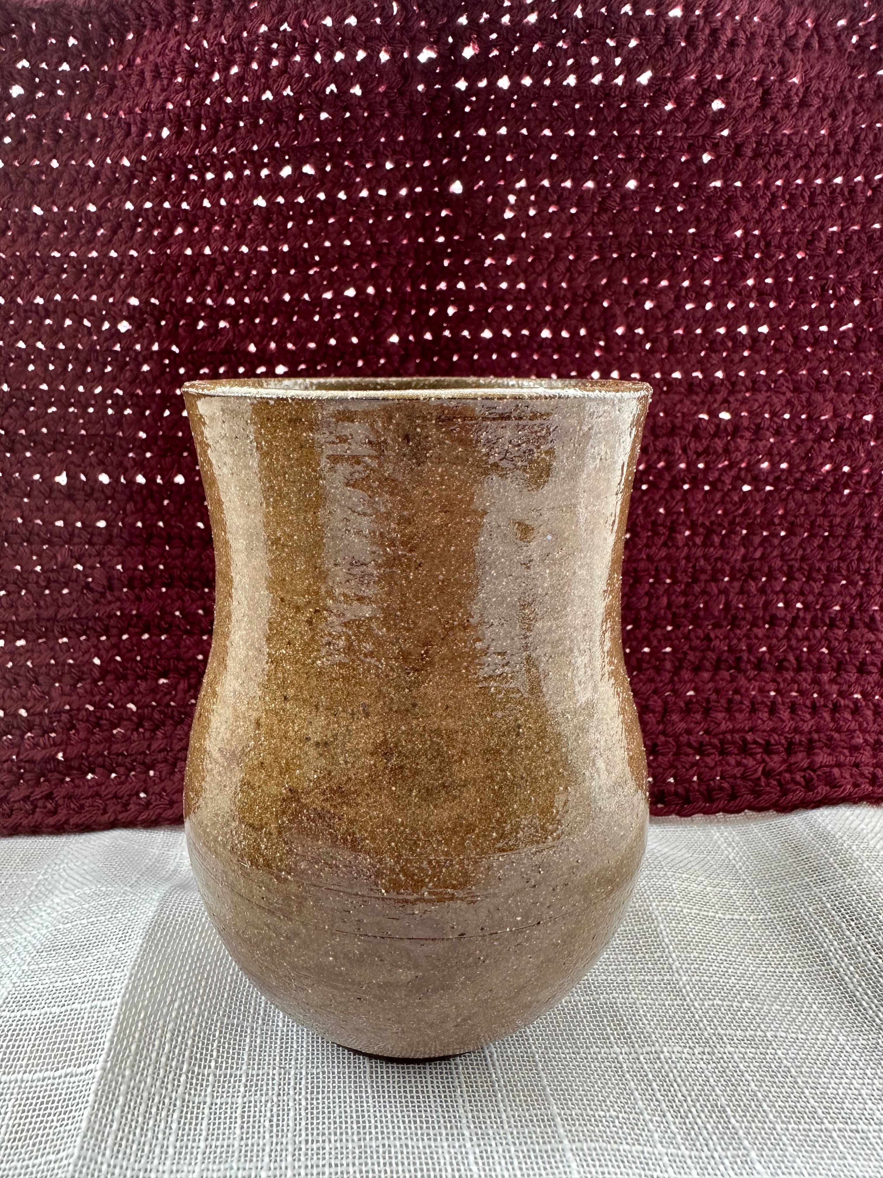 Brown ceramic vase on a textured surface with a maroon fabric background