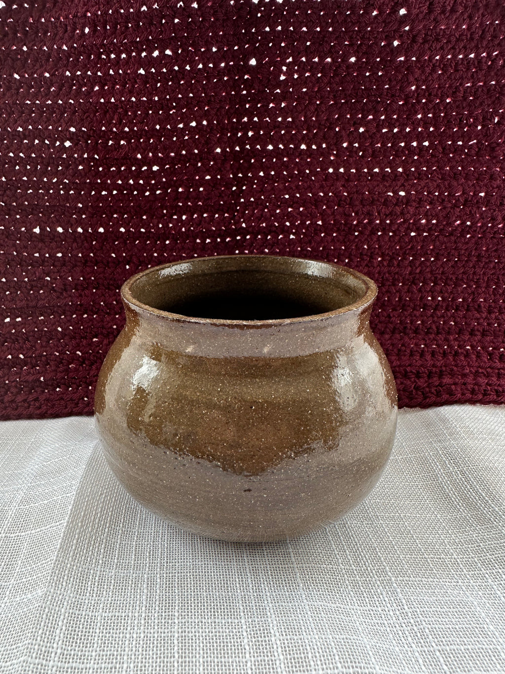 Brown ceramic pot on a textured surface with a maroon fabric background