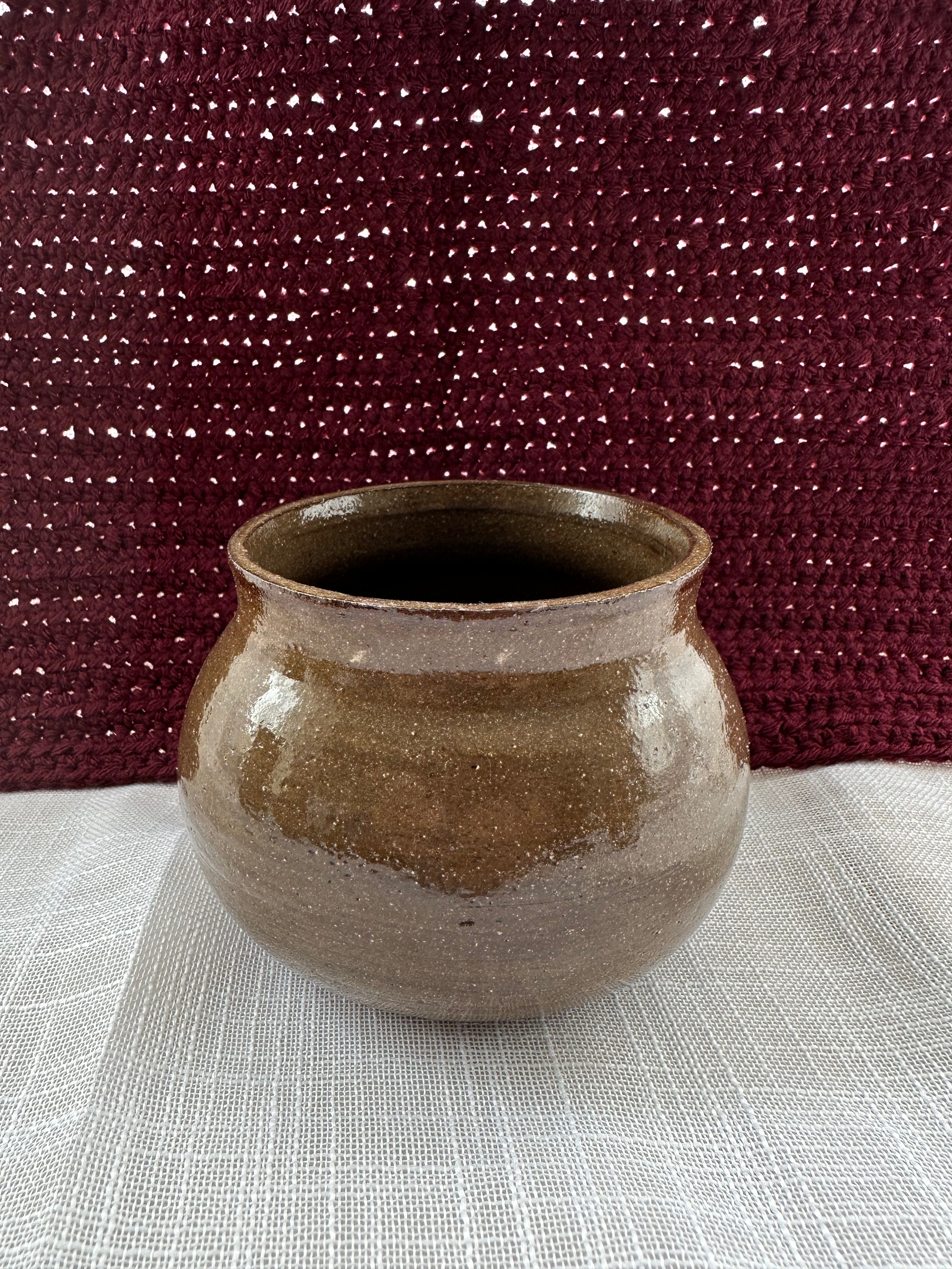 Brown ceramic pot on a textured surface with a maroon fabric background