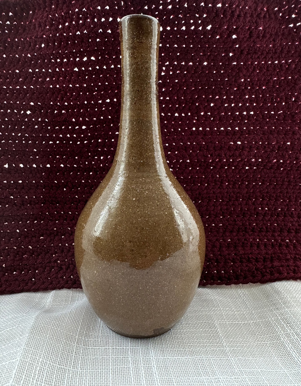 Brown ceramic vase on a textured surface with a dark fabric background