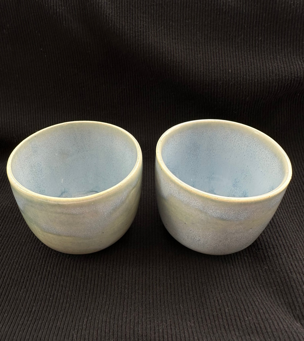 Two ceramic cups with a textured surface on a black background
