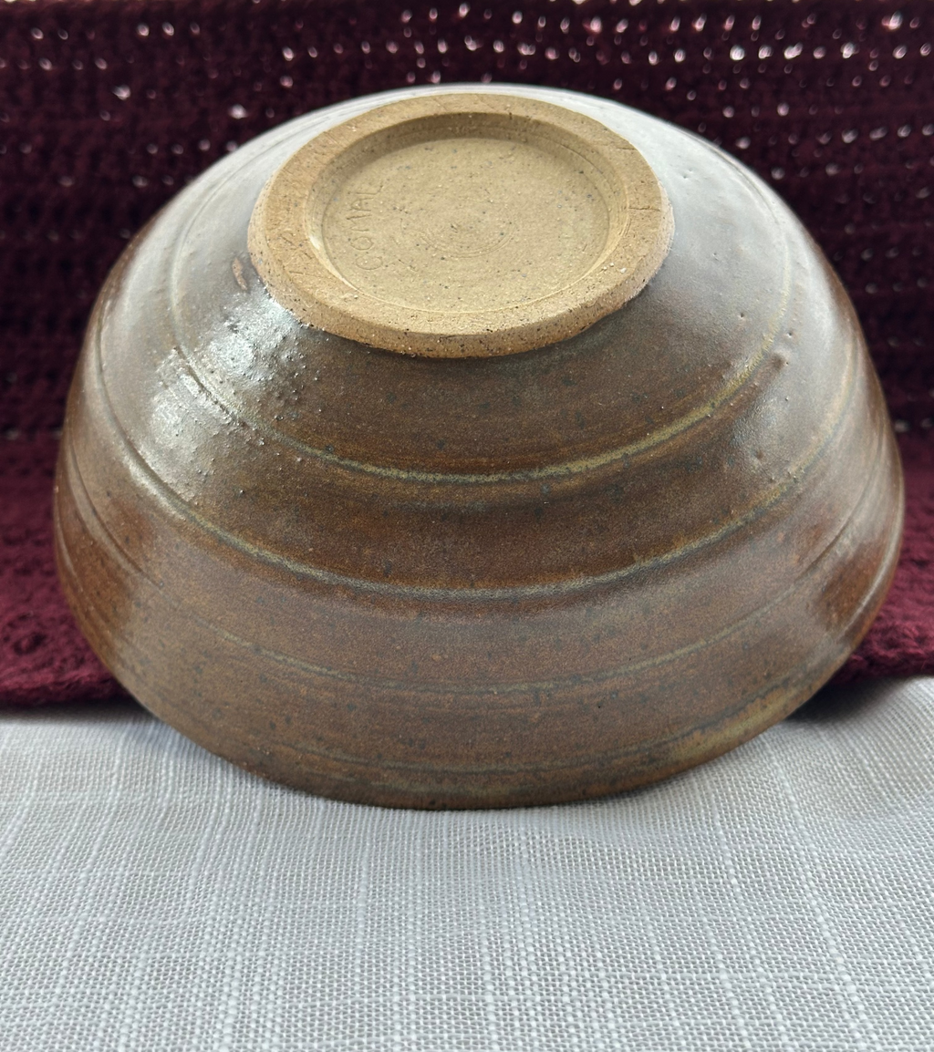 Brown ceramic bowl on a textured surface with a maroon woven mat in the background