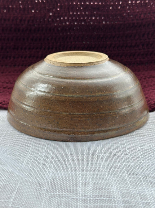 Brown ceramic bowl on a textured surface with a dark fabric background