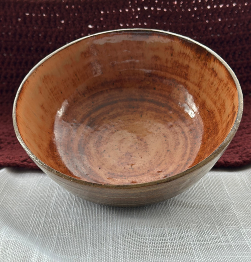 Brown ceramic bowl on a textured surface with a woven mat in the background