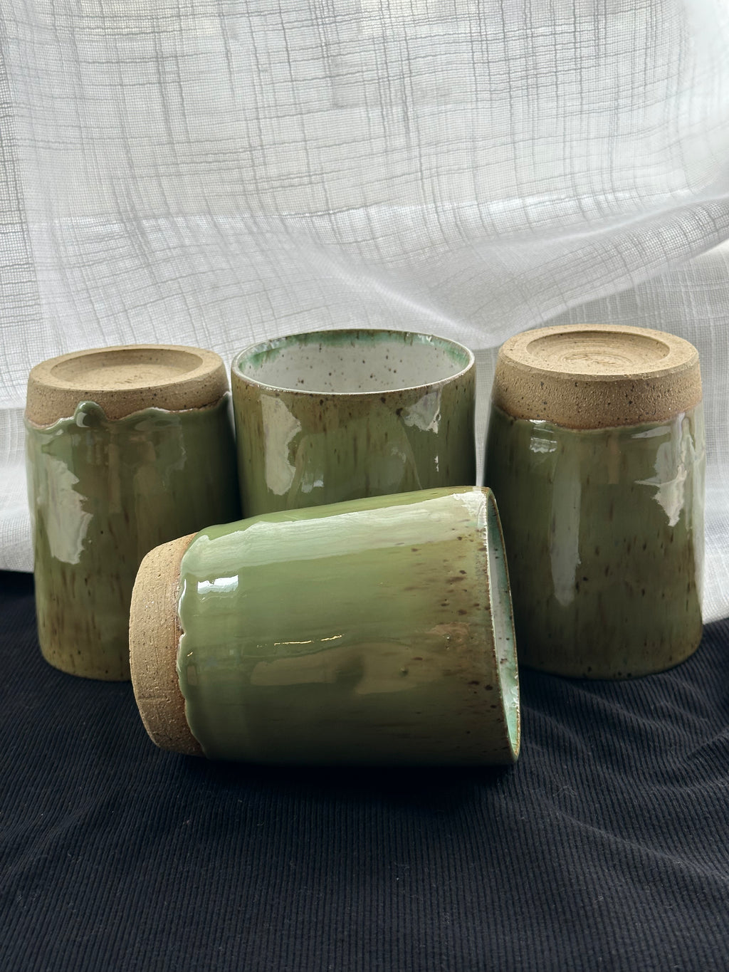 Four green ceramic cups on a dark surface with a white fabric background