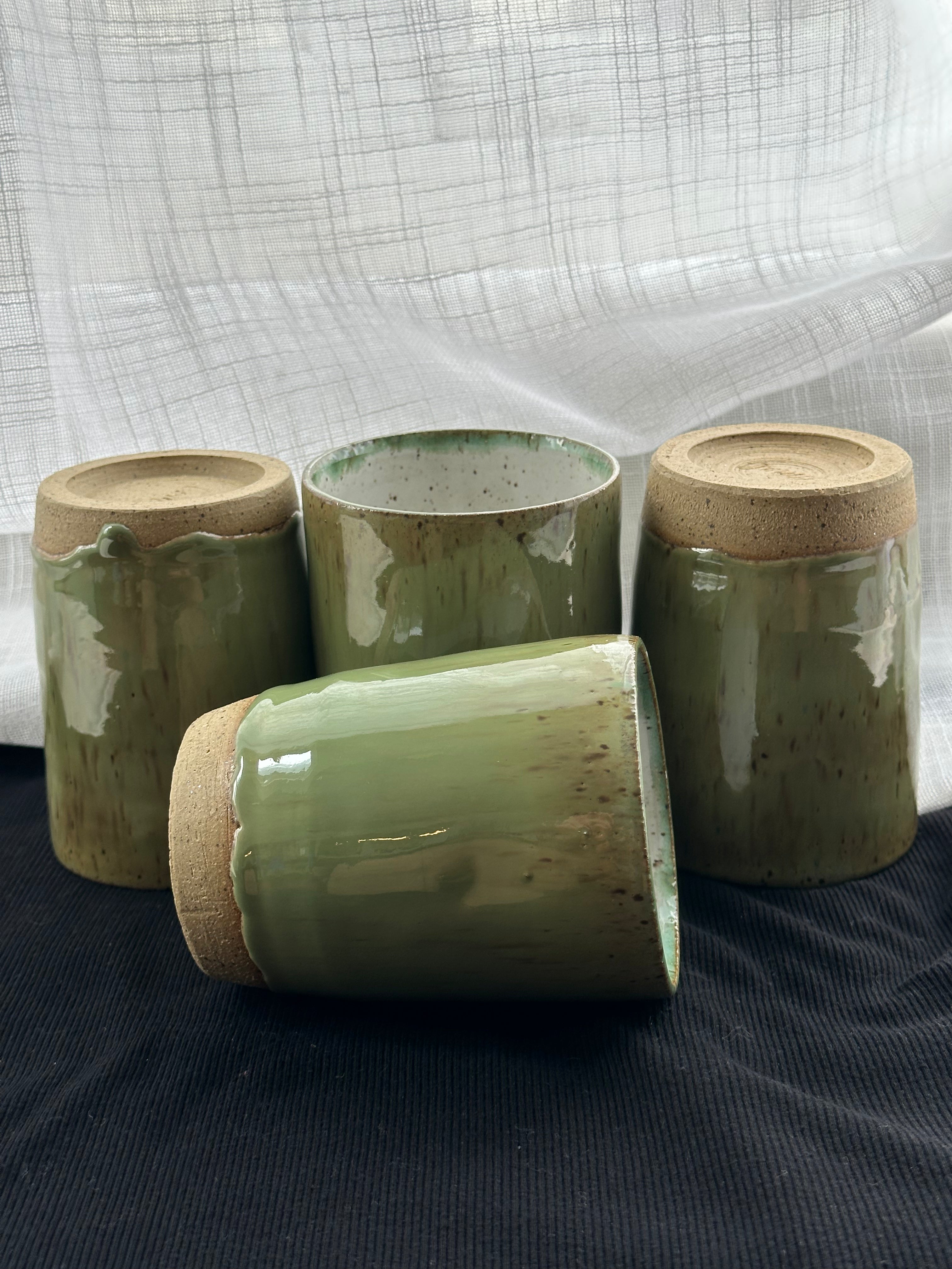 Four green ceramic cups on a dark surface with a white fabric background
