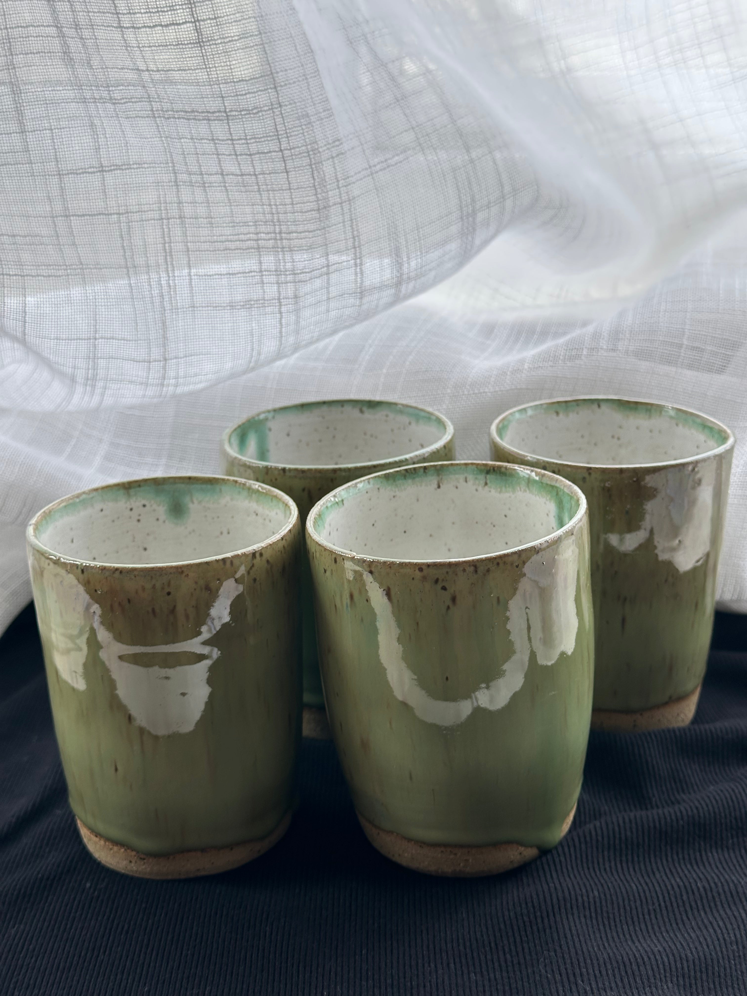 Set of four green ceramic cups with white accents on a dark surface.