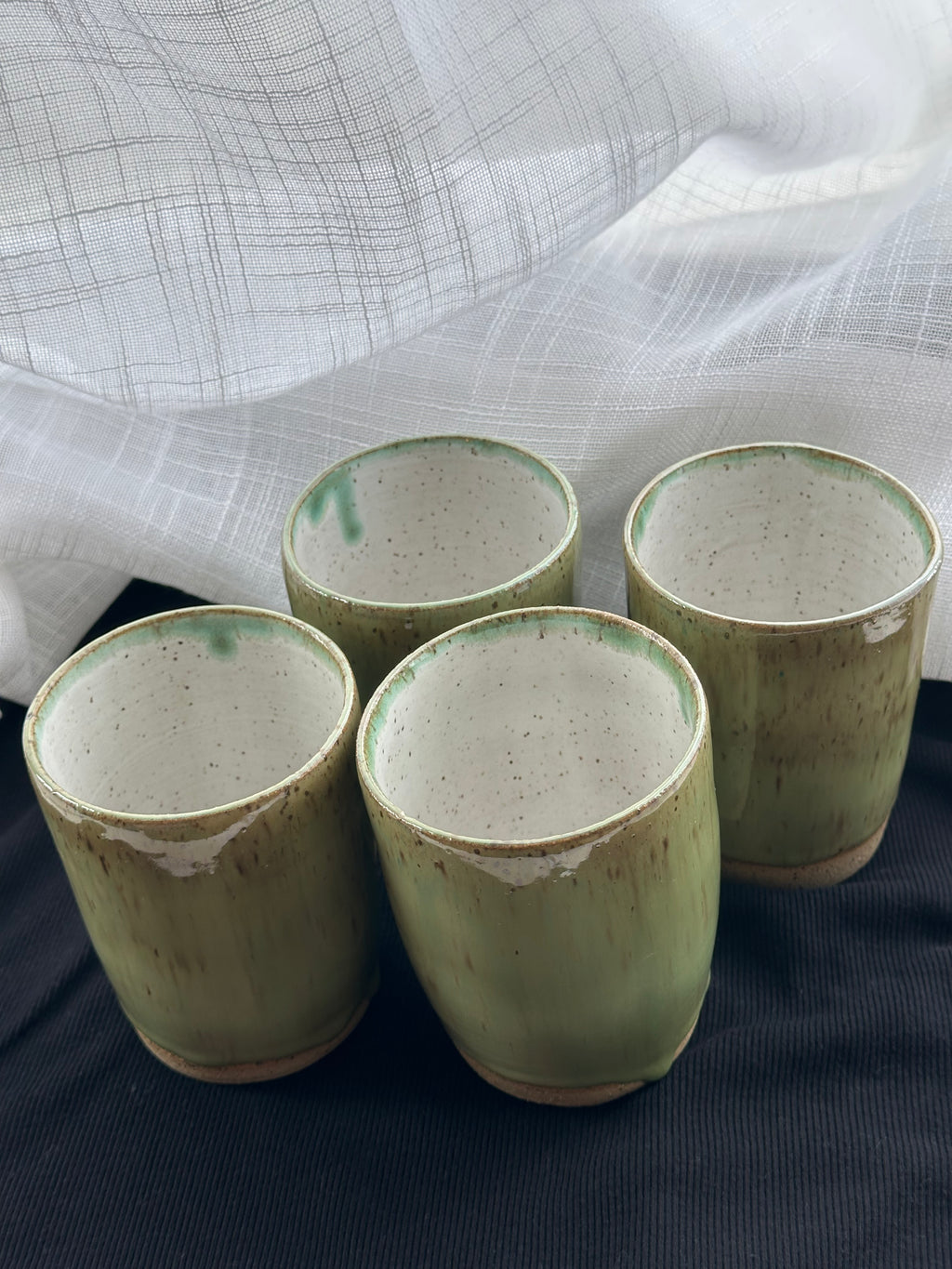 Four green ceramic cups on a dark surface with a light fabric background
