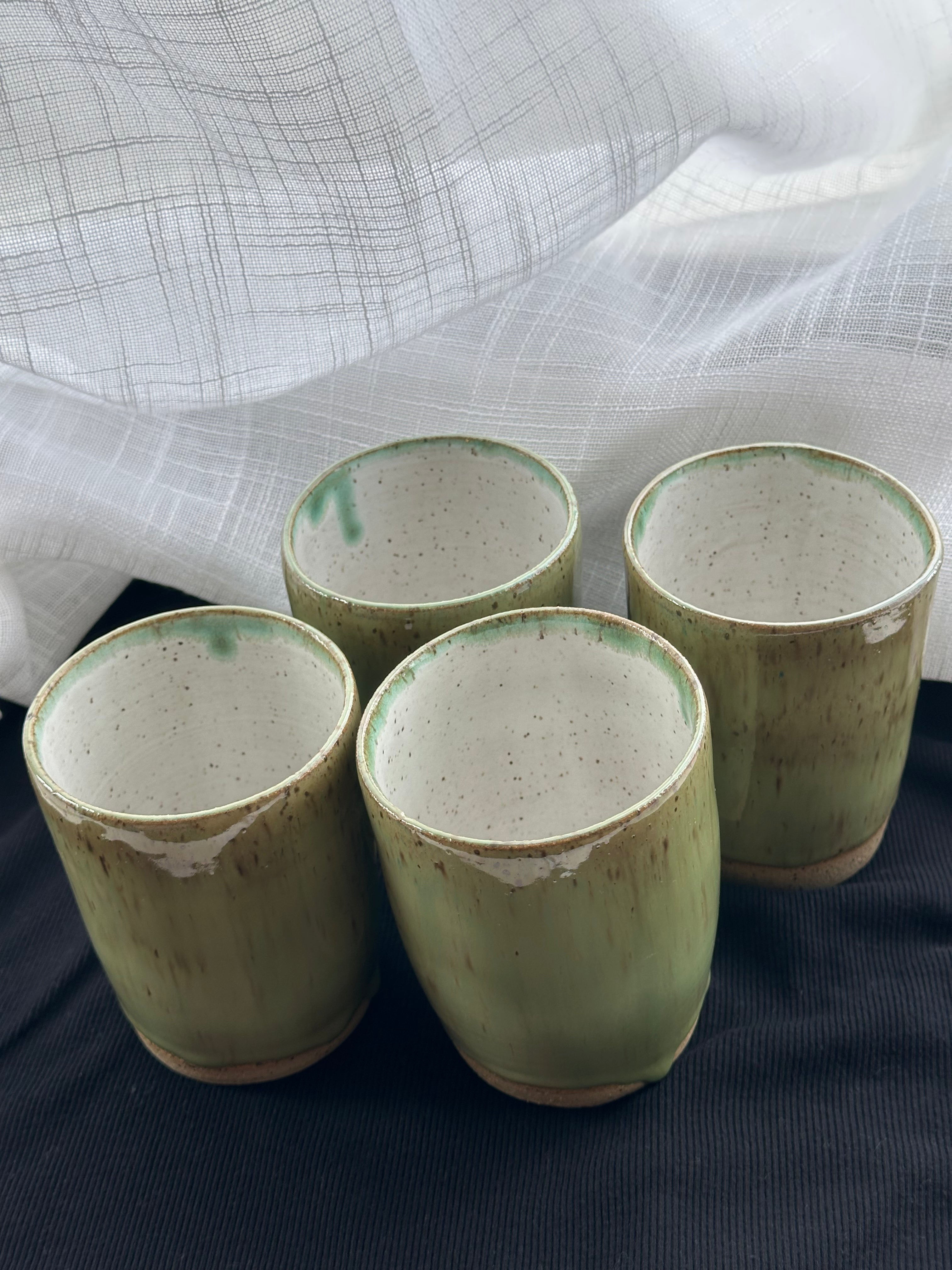 Four green ceramic cups on a dark surface with a light fabric background