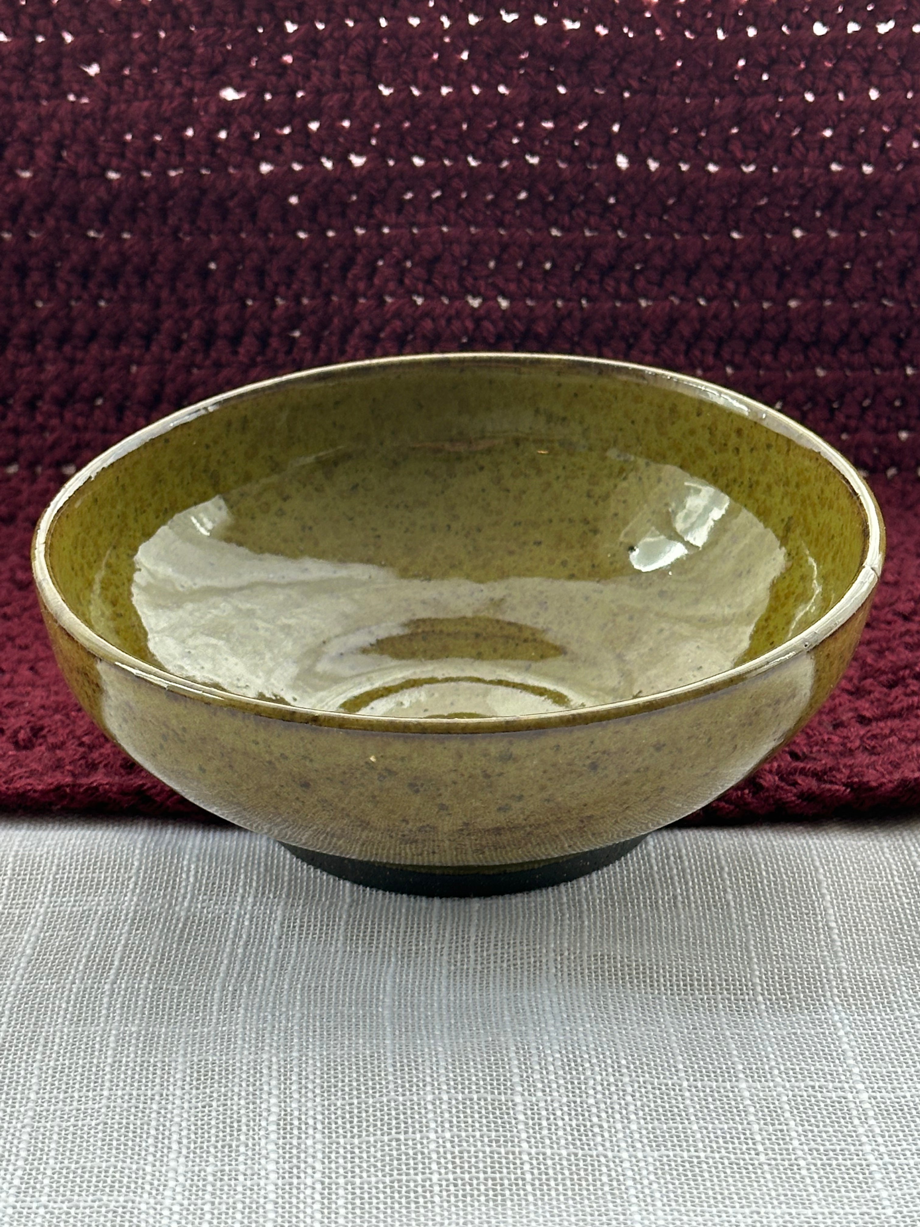 Green ceramic bowl on a textured surface with a maroon fabric background