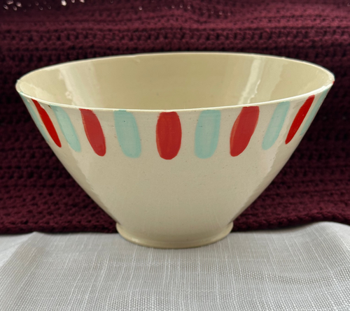 Beige ceramic bowl with red and blue stripes on a textured surface with a maroon fabric background