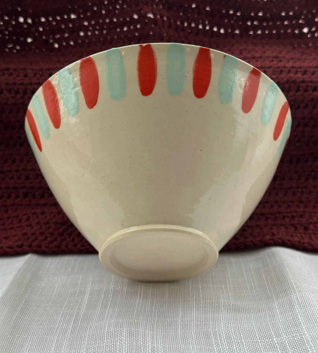 Ceramic bowl with red and green stripes on a textured surface