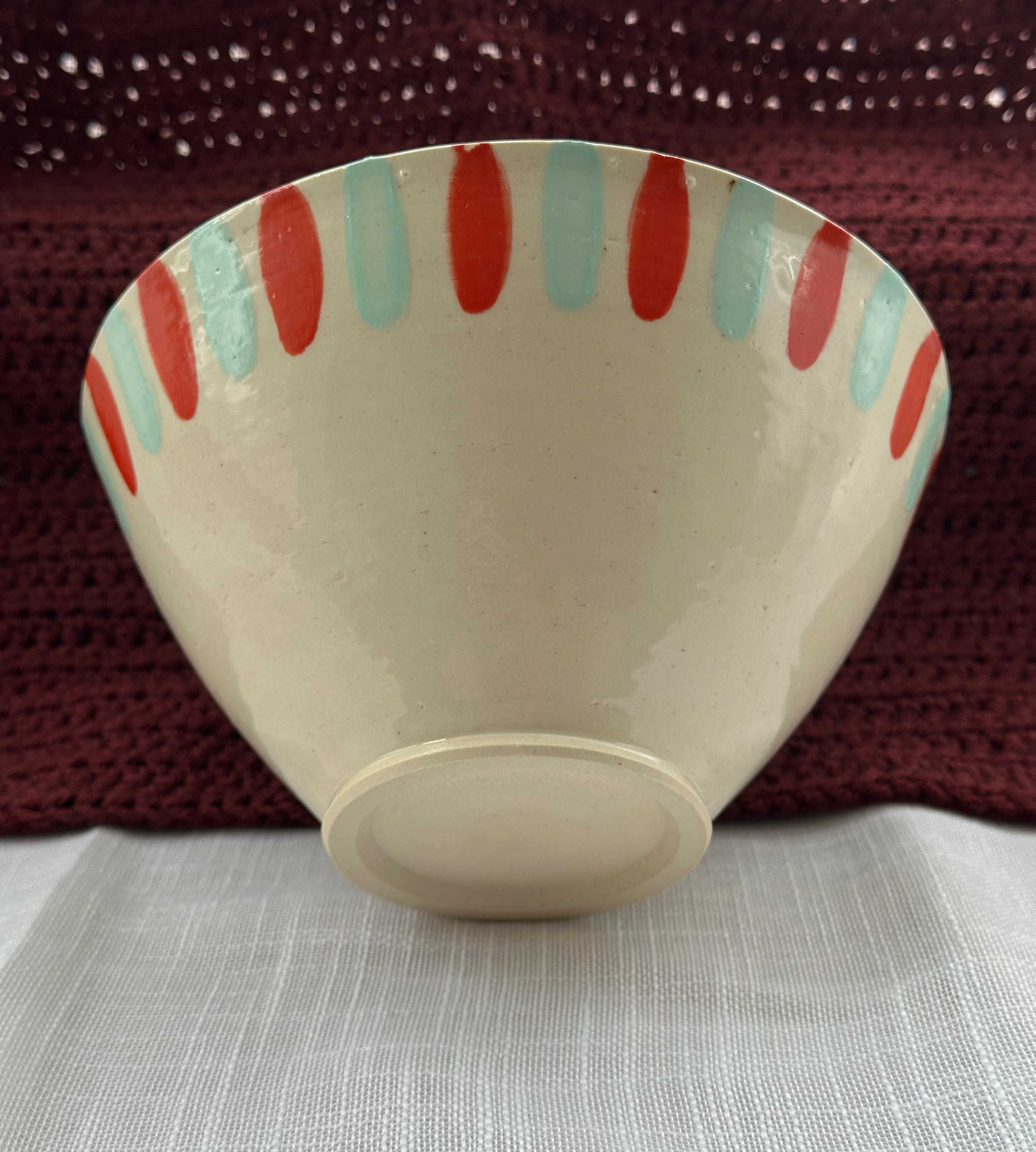 Ceramic bowl with red and green stripes on a textured surface