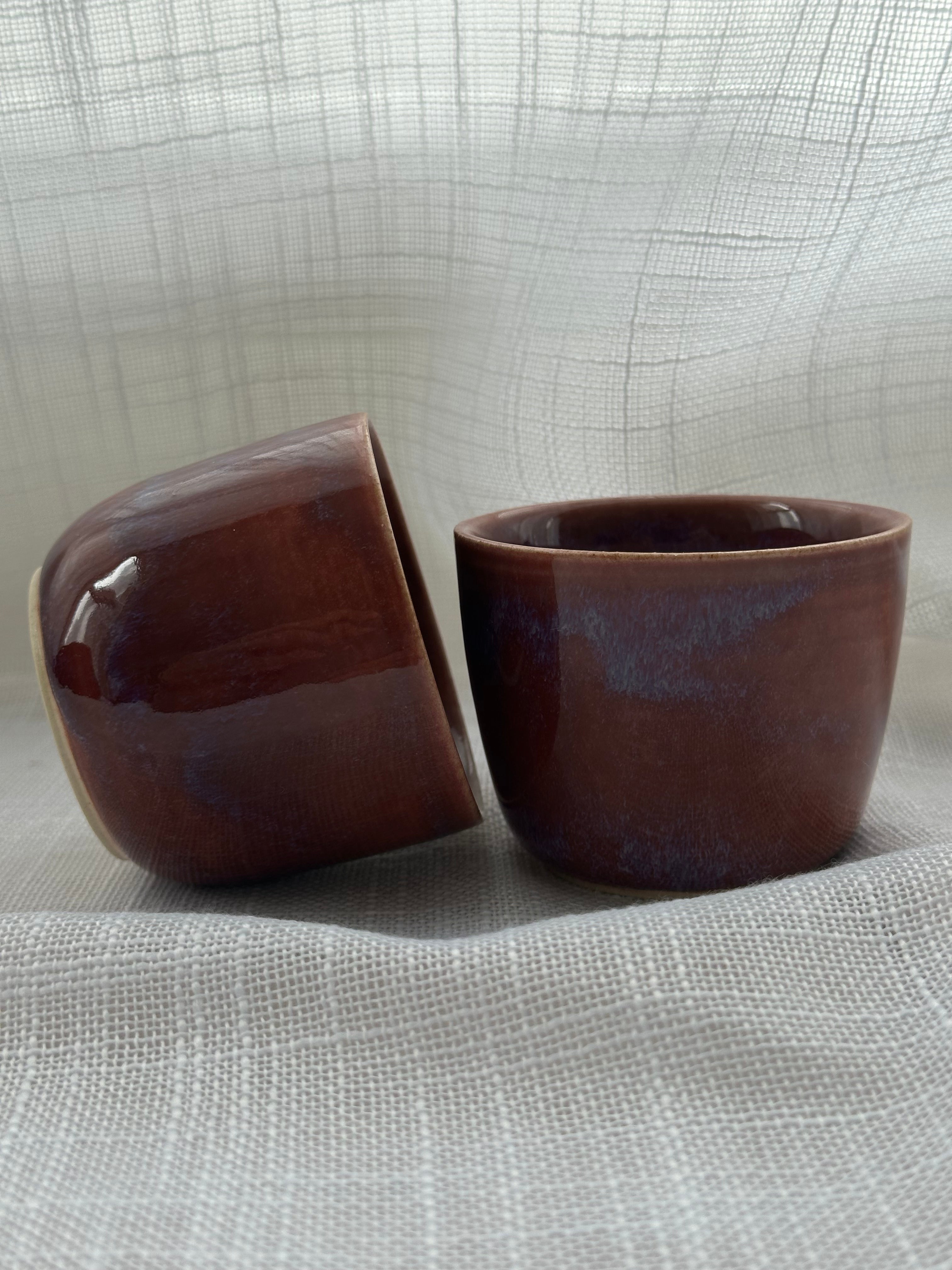 Two brown ceramic cups on a textured gray surface