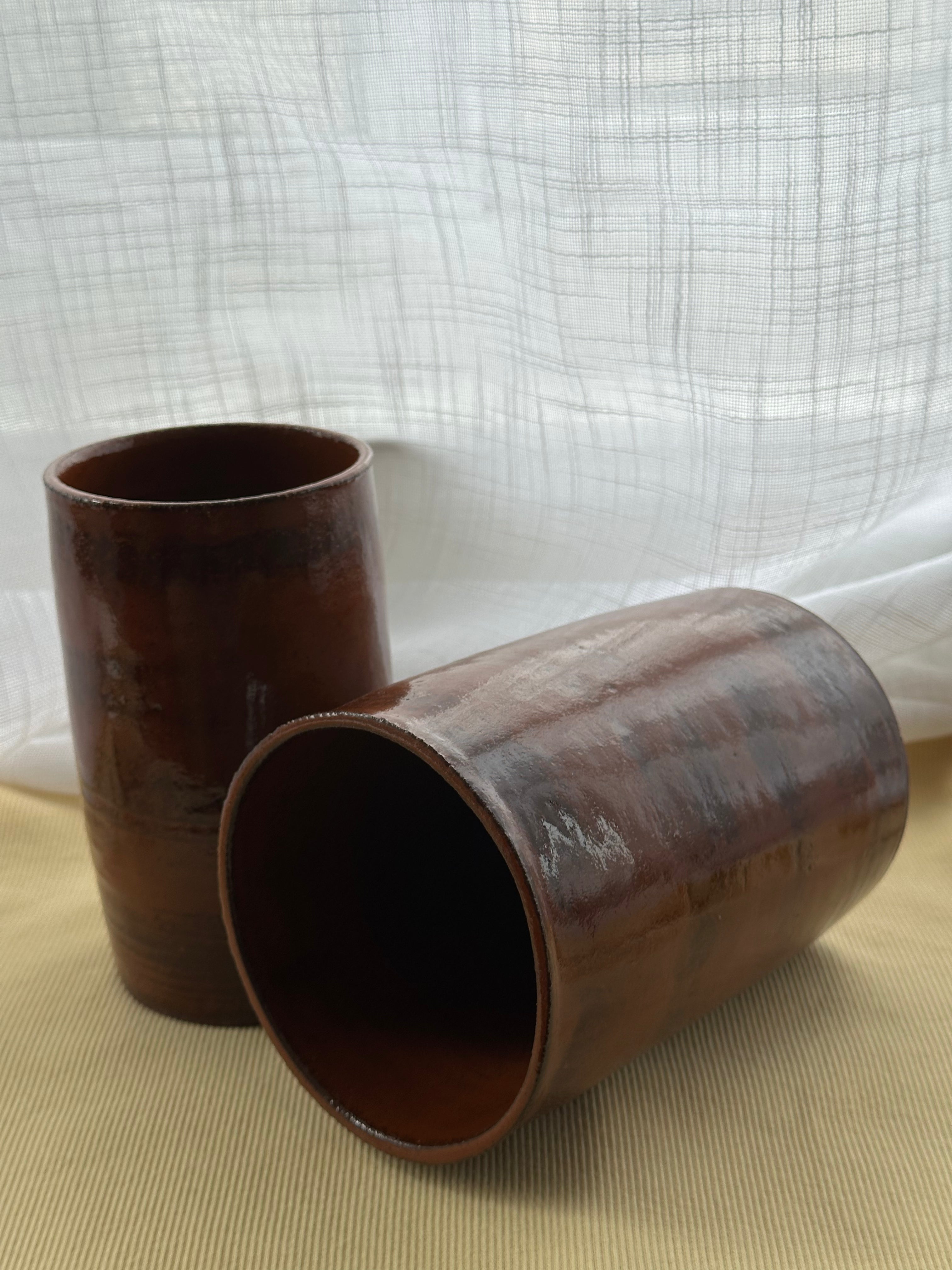 Two rustic cylindrical vases on a beige surface with a white textured background