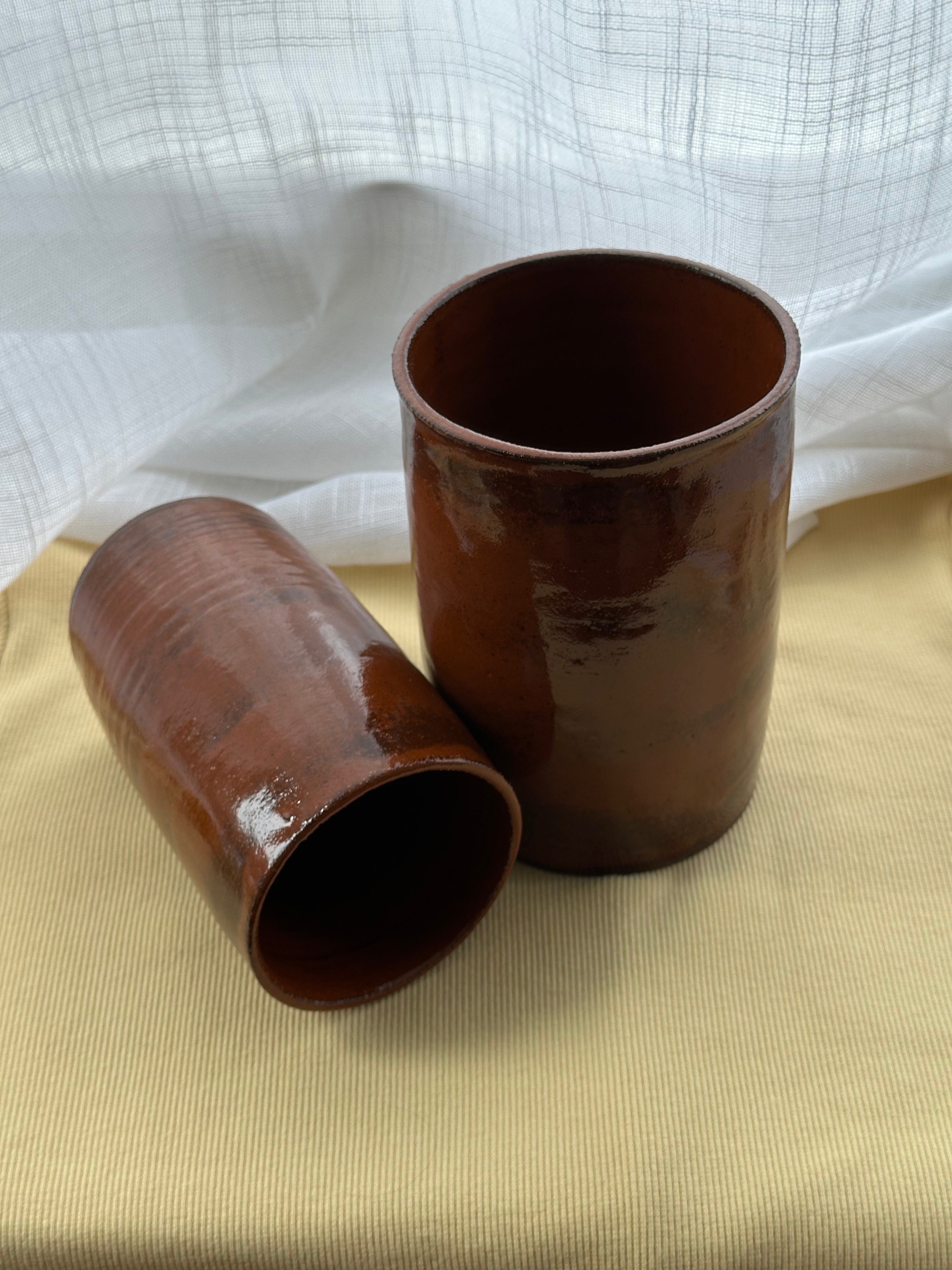 Two rustic cylindrical vases on a beige surface with a white textured background