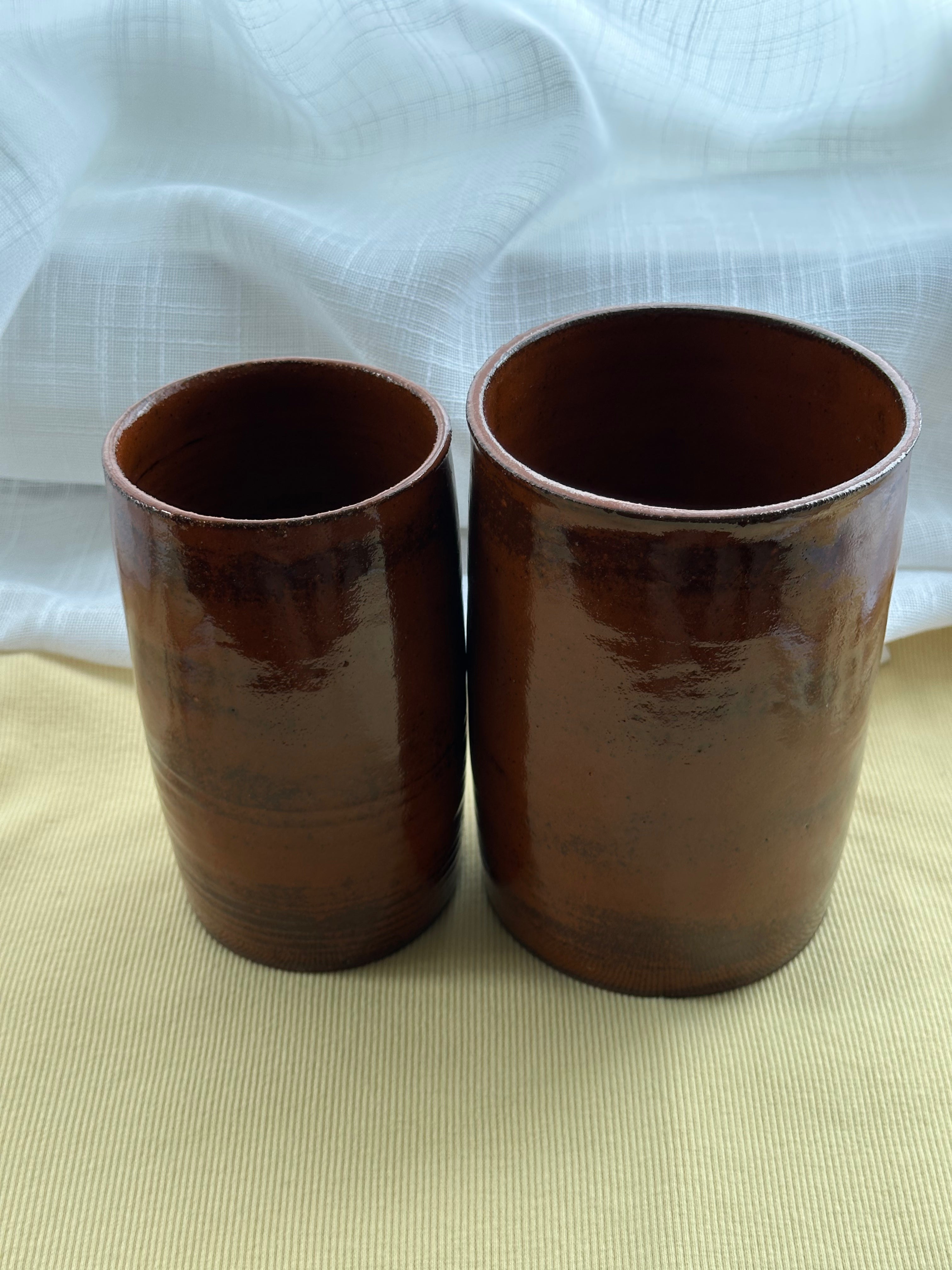 Two rustic cylindrical vases on a beige surface with a white textured background