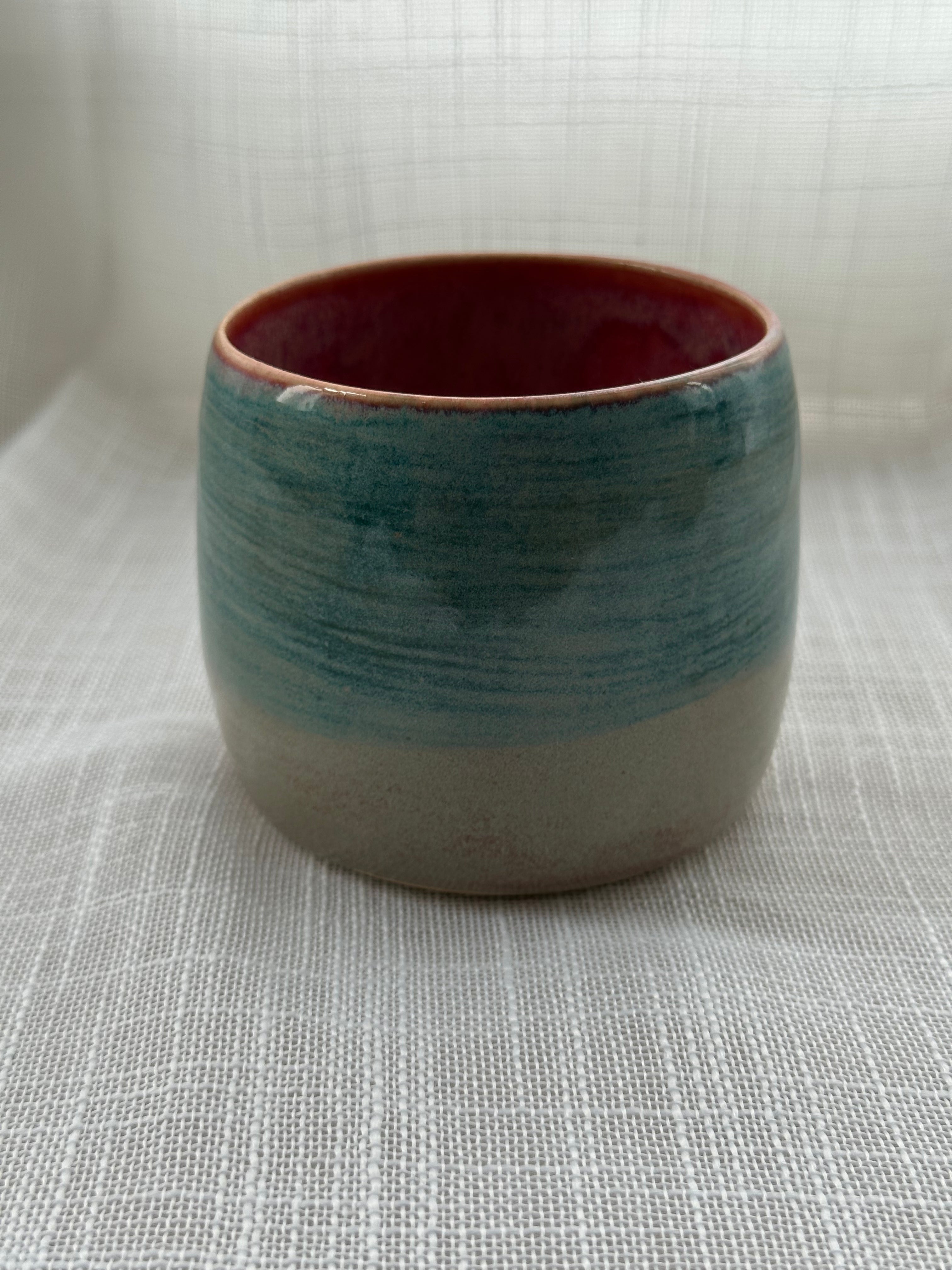 Ceramic cup with a gradient color from teal to gray on a textured surface