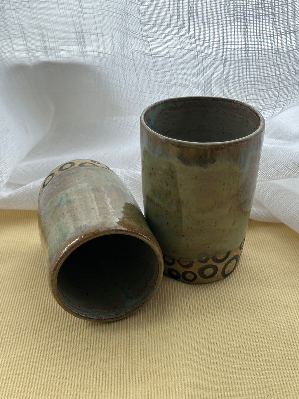 Two ceramic cups with a textured surface on a beige surface with a white fabric background