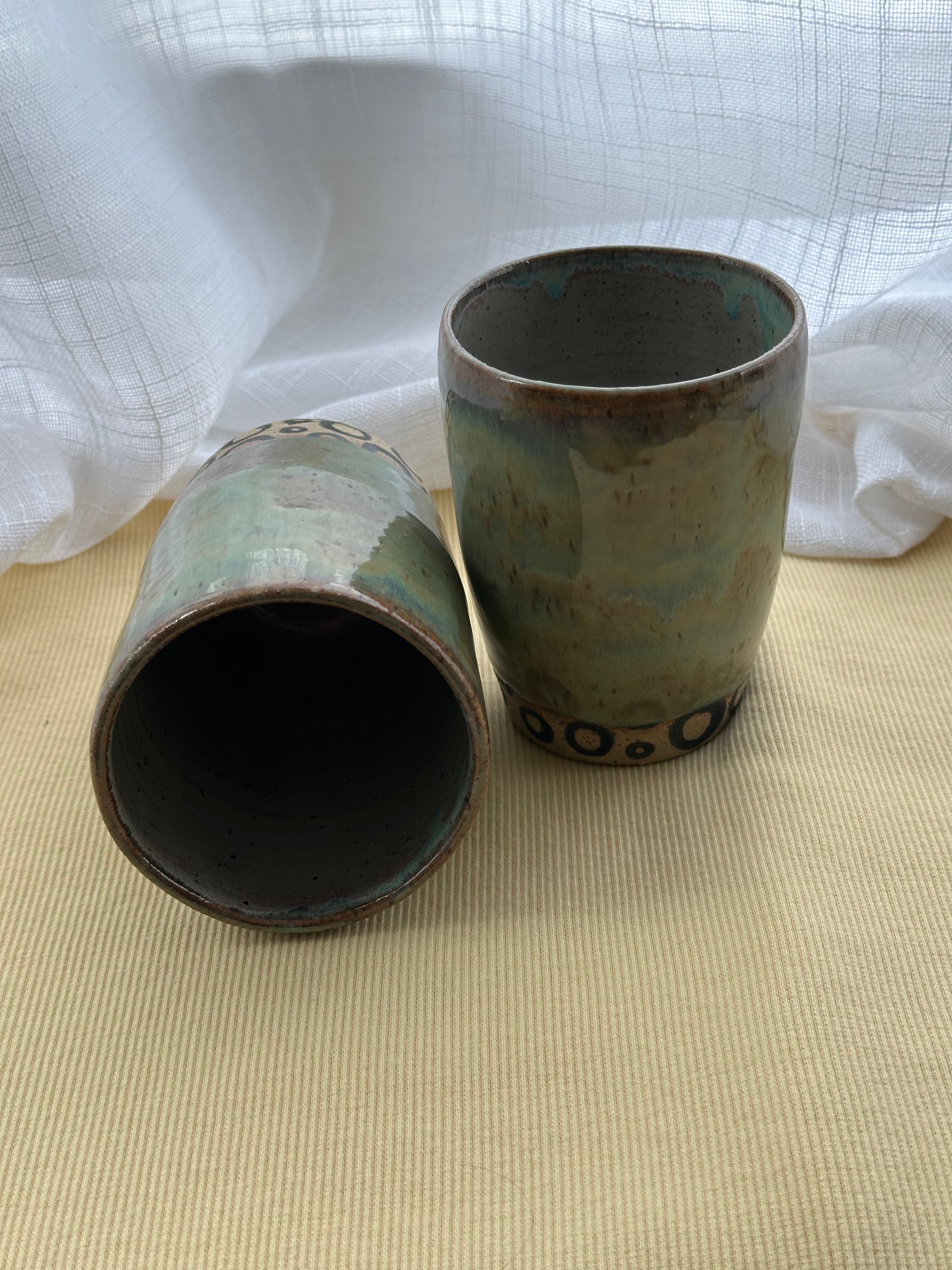 Two ceramic cups with a textured surface on a beige surface with a white cloth background.