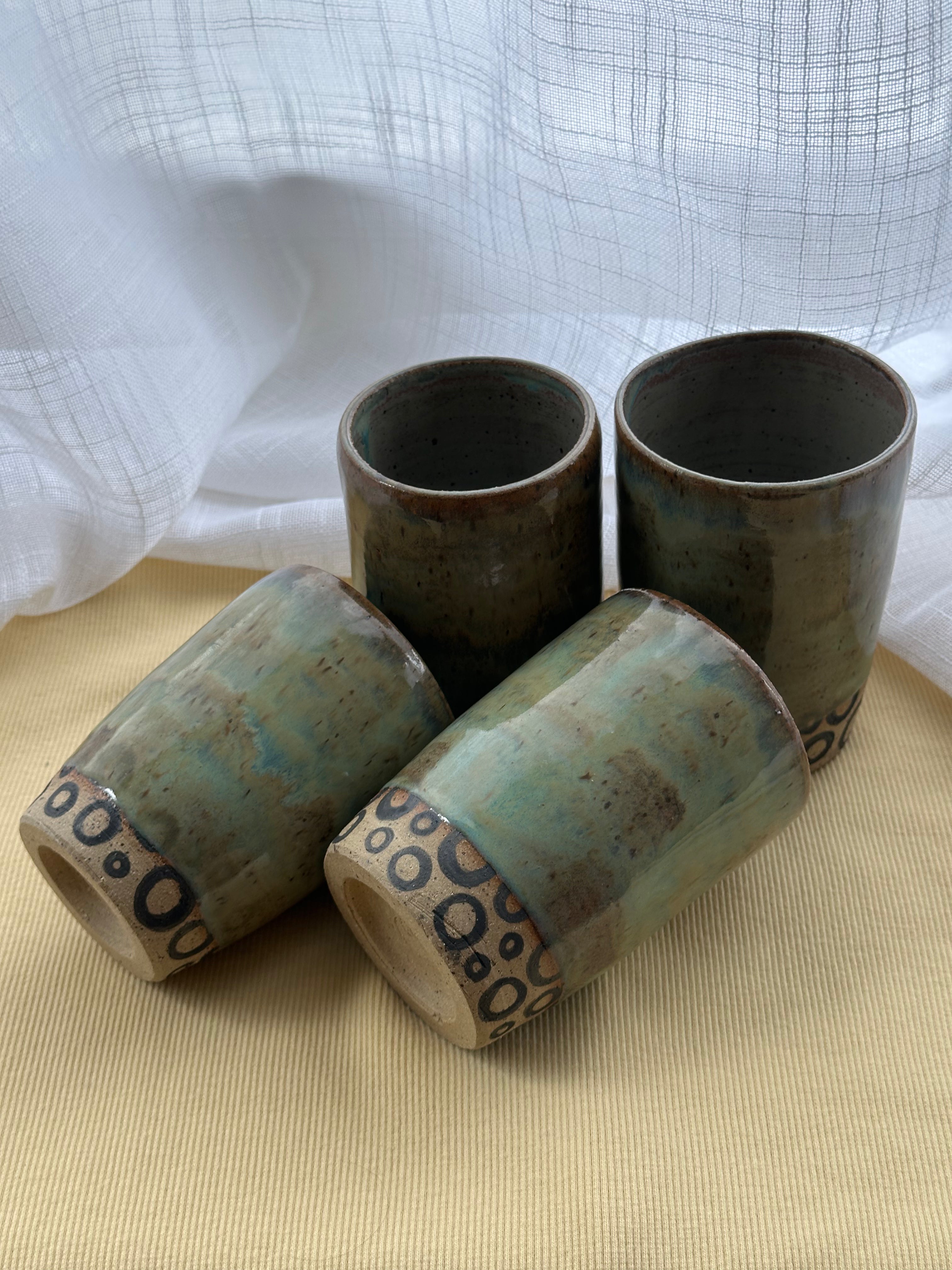 Four ceramic cups with textured design on a beige surface and white fabric background