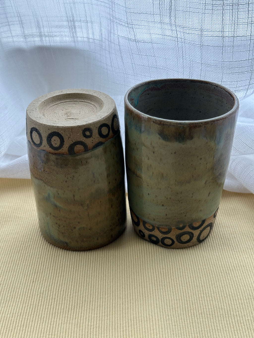 Two ceramic containers with decorative patterns on a beige surface and white background
