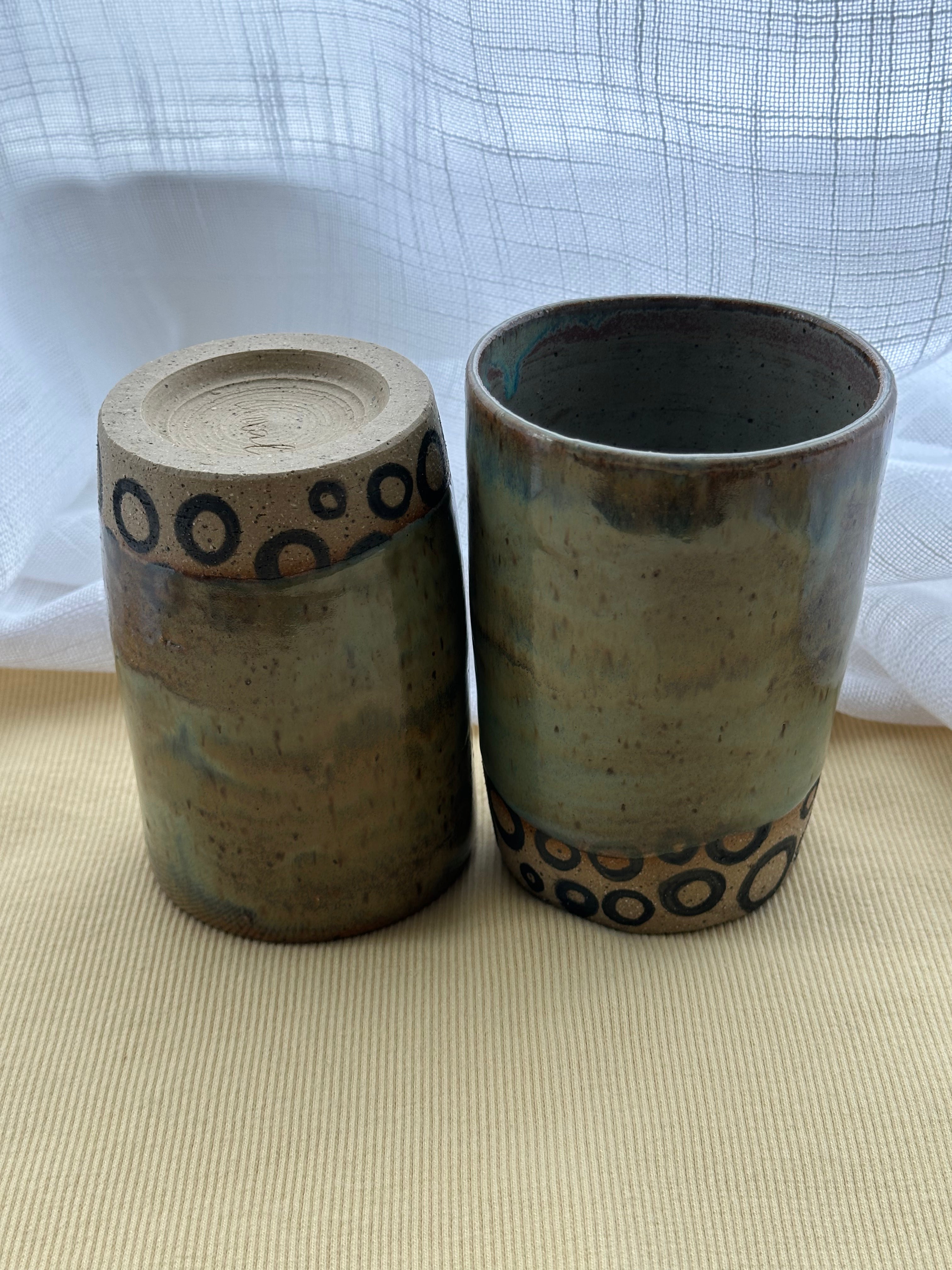 Two ceramic containers with decorative patterns on a beige surface and white background