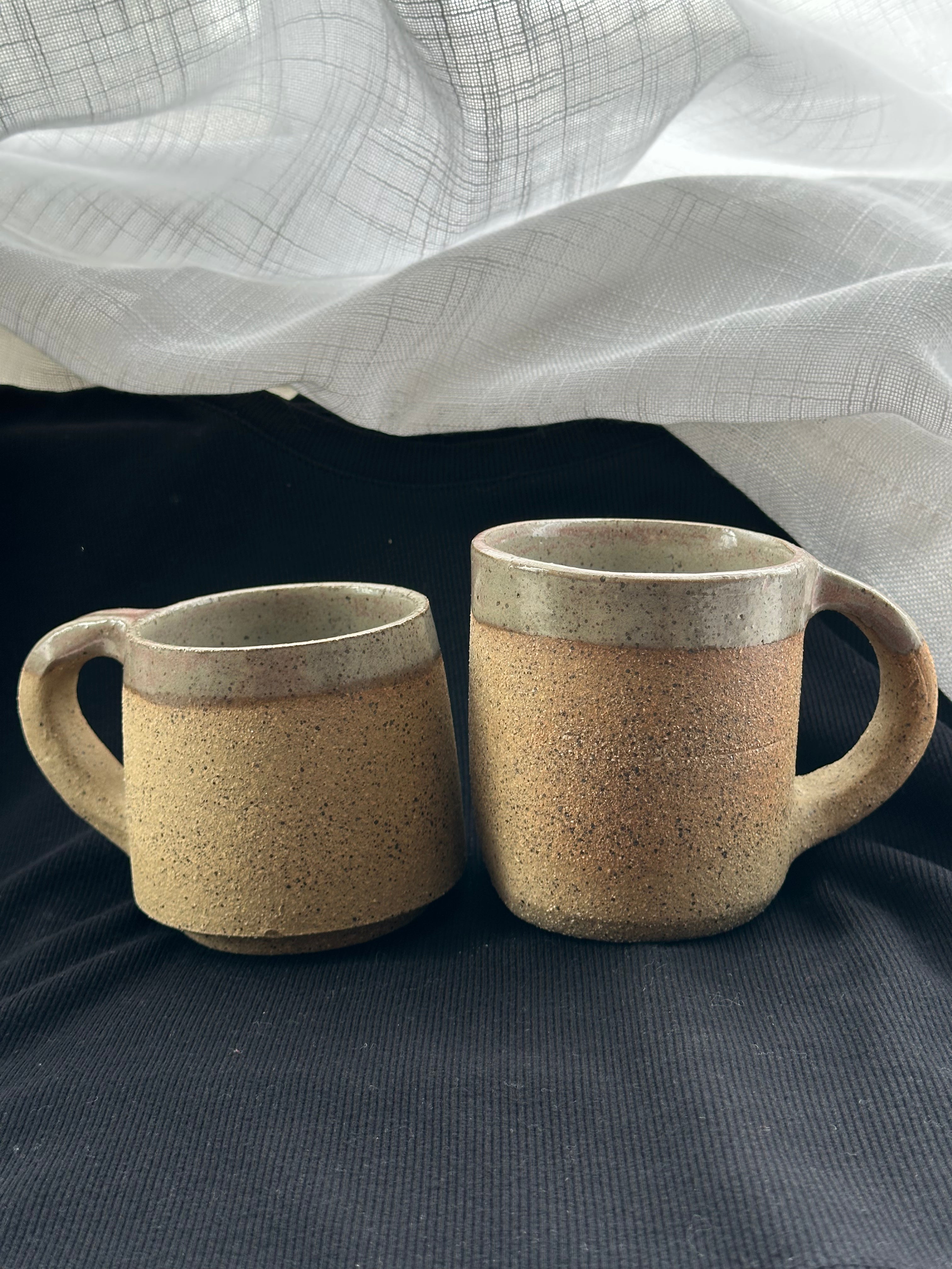 Two ceramic mugs with textured finish on a dark fabric background